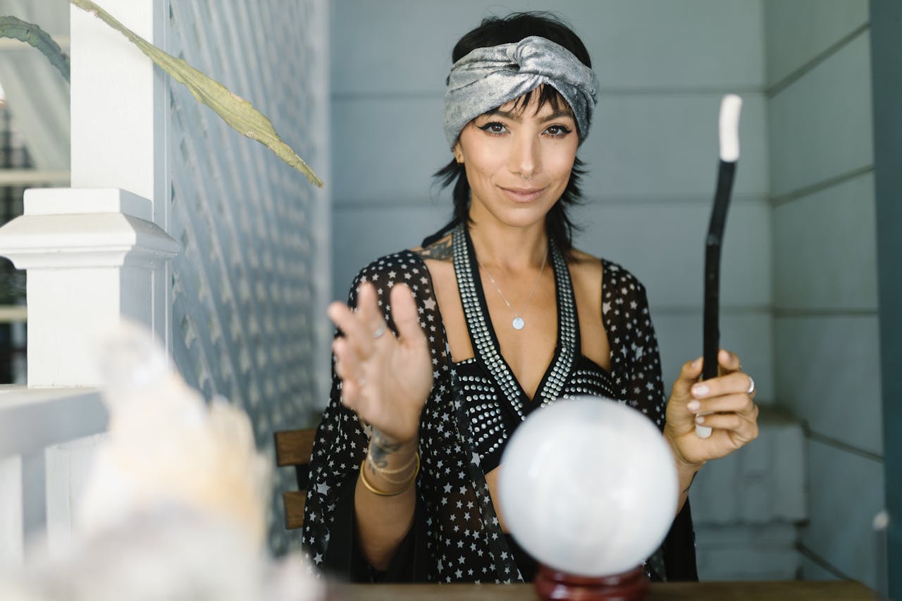A woman in a headband performs a mystical ritual with a crystal ball and wand.