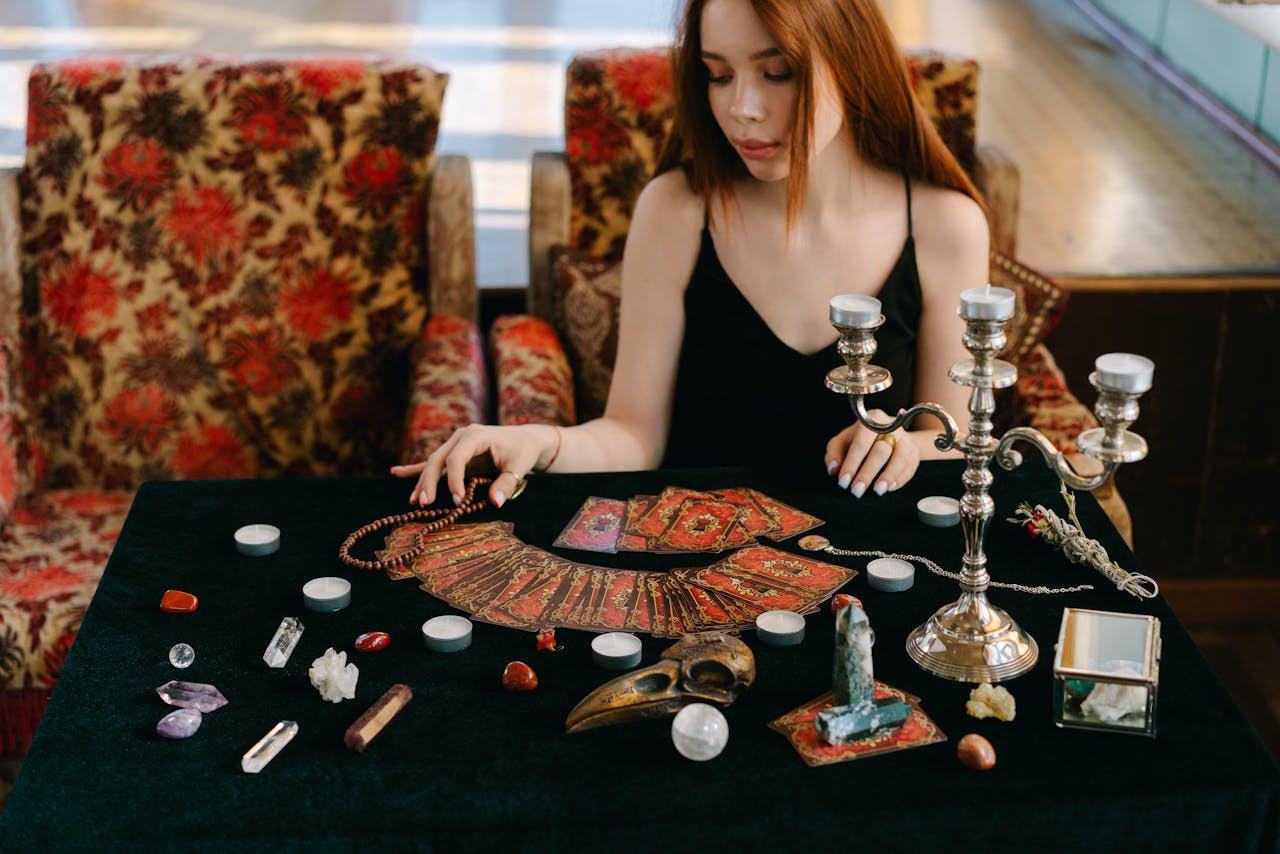 Mystical scene with a woman reading tarot cards surrounded by gemstones and candles.